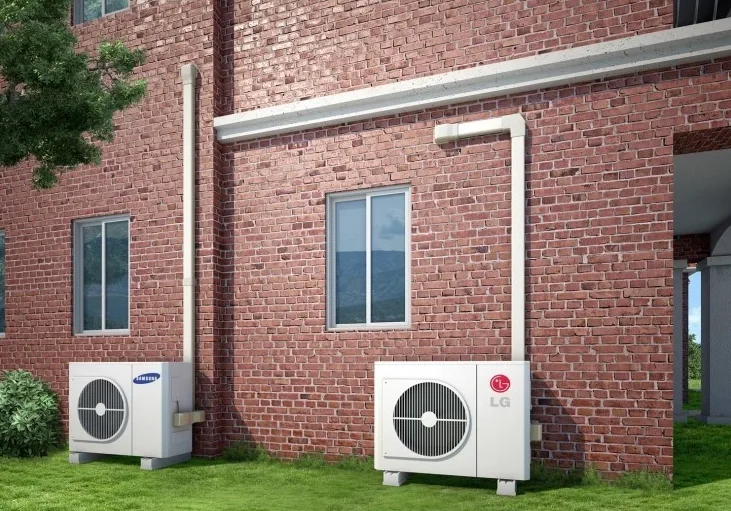 Two outdoor condensing units on pads beside a building, refrigerant piping run up the wall in covered trunking